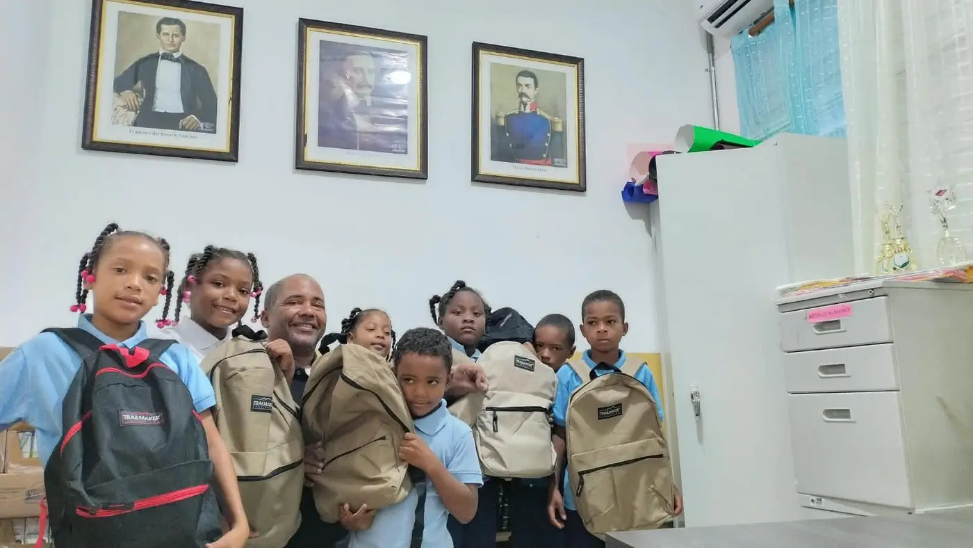 Children and a community volunteer with donated backpacks